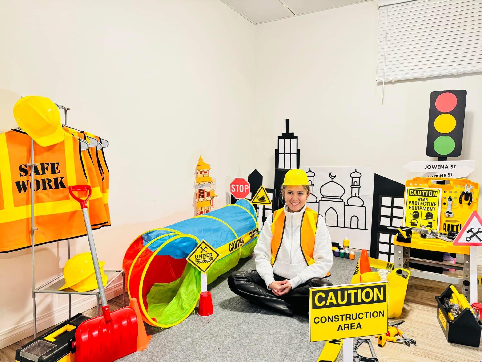 Jowena kneeling in a hard hat and safety vest inside a hand-built cardboard construction site
